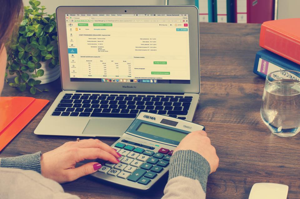 Finance officer reconciling accounts on a calculator and laptop
